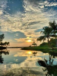 una puesta de sol sobre un cuerpo de agua con palmeras en Marari Beach Pearl Homestay, en Mararikulam
