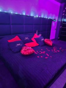 ein violettes Bett mit lila Kissen und rosafarbener Beleuchtung in der Unterkunft Les Secrets Rooms in Hagondange