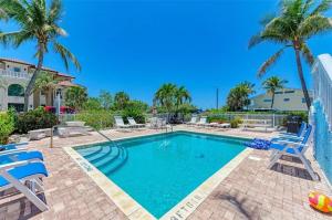 a swimming pool with two chairs and palm trees at Anna Maria Island Beach Front Condo - 50 steps to Beach in Holmes Beach