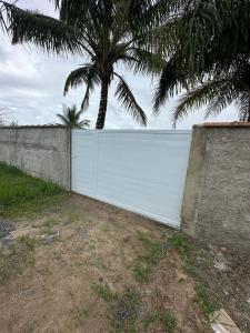 a white fence with a palm tree behind it at Pé na areia in Ilha Comprida