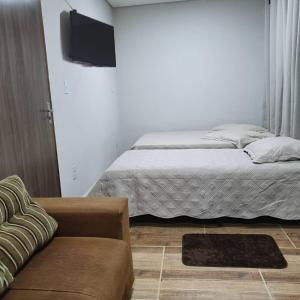 a bedroom with a bed and a couch and a tv at Suítes Nativa STL in São Thomé das Letras