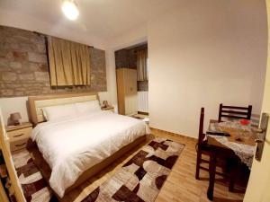 a bedroom with a white bed and a table and a desk at Bujtina Argis Voskopoje in Voskopojë