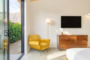 a bedroom with a yellow chair and a television at Blackhaus B10 by AvantStay Modern Room Pool in Palm Springs