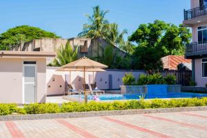 a swimming pool with an umbrella and a house at Ais apartments in Zanzibar City