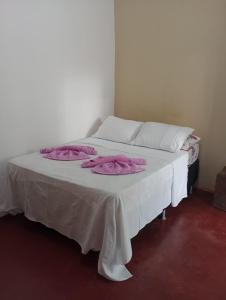 a bed with white sheets and pink towels on it at Chalé da Vânia in Alto Paraíso de Goiás