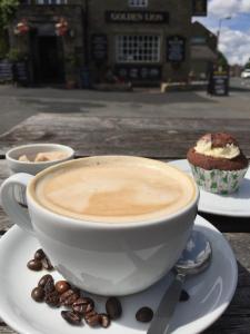 a cup of coffee and a cupcake on a table at Old Coach House At The Golden Lion in Saint Johns Chapel