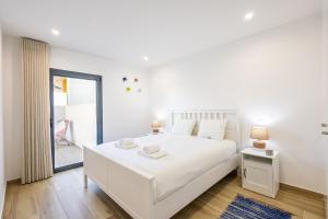 a white bedroom with a large white bed and a window at Baia Mar T1 - By Smarthomes in São Martinho do Porto +33 photos
