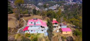 een groot huis met een roze dak op een heuvel bij The City Escape Farmstay in Shimla
