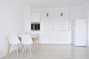 a kitchen with white cabinets and a table and white chairs at Cozy Apartment with private parking in Piešťany