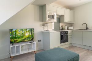 a kitchen with white cabinets and a flat screen tv at Prime Stay Apartments in Paisley