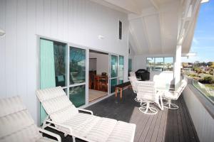 a porch with white chairs and a table on a deck at Tindalls Bay Beach House in Whangaparaoa