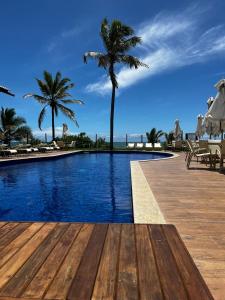 ein Swimmingpool mit Palmen und dem Meer in der Unterkunft Village Itacimirim Boulevard - Pé na areia in Itacimirim