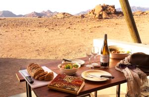 a table with food and a bottle of wine and wine glasses at Desert Quiver Camp in Sesriem