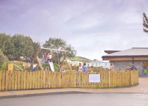 a group of people playing on a playground behind a wooden fence at Sunbeach Holiday Park in Llwyngwril