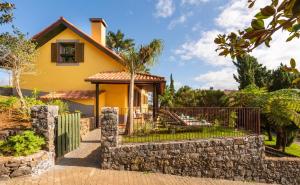 a yellow house with a fence and a stone wall at Hotel Quinta Do Furao in Santana