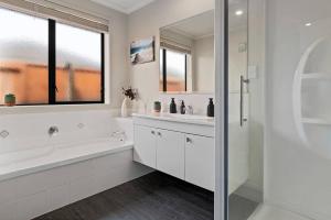 a white bathroom with a tub and a sink and a shower at A Beach Hive at Papamoa Beach - 4 bedrooms in Papamoa +23 photos