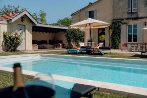 a swimming pool with chairs and a table and an umbrella at Maison Groleau in Mombrier