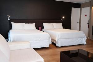 two beds with white sheets in a room with a couch at Amérian Córdoba Park Hotel in Córdoba
