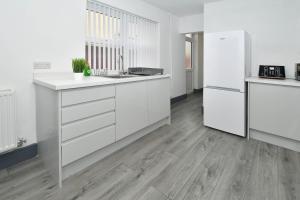 a kitchen with white cabinets and a wooden floor at Townhouse @ Eastwood Place Stoke in Etruria