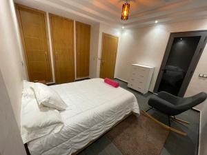 ein Schlafzimmer mit einem weißen Bett und einem schwarzen Stuhl in der Unterkunft Résidence villa in Agadir