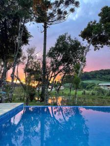 a swimming pool with a sunset in the background at Casa de campo com piscina em meio à natureza in Campo Magro