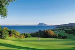Ein Mann steht auf einem Golfplatz mit dem Meer im Hintergrund in der Unterkunft COSTA by Hawkins BajoA in Algeciras