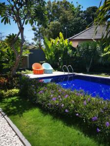 a swimming pool in a garden with purple flowers at Amuya Home Stay in Waingapu