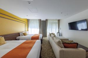 a hotel room with two beds and a couch and a tv at WeBase KAMAKURA in Kamakura