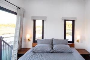 a bed in a bedroom with two windows at The Farmer Farm Stay & Cafe in Chom Thong