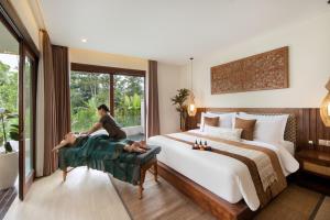 a bedroom with a large bed with two people sitting on a couch at Khastana Hadi Tegallalang, Ubud in Tegalalang