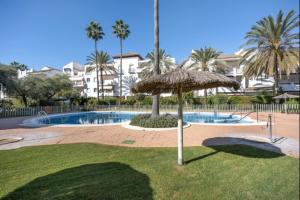 a pool with an umbrella and palm trees and buildings at Paraíso del golf free parking by Staycare in Rota