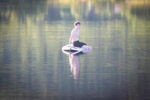 Ein Junge, der auf einem Surfbrett im Wasser sitzt. in der Unterkunft Arctic photo retreat Lofoten - lakehouse Bjørkly in Vestvågøya + 63 Fotos