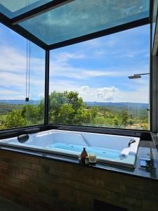 una vasca da bagno in una stanza con una grande finestra di Khaya Chalés - Chalés de Luxo na Serra para Casais com Hidro a Jaboticatubas
