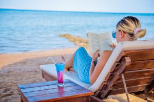 Caves Beach Resort Adults Only في الغردقة: امرأة تجلس على كرسي تقرأ كتاب على الشاطئ +37 صورة