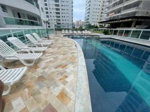 a swimming pool with white lounge chairs next to a building at Apartamento completo no Centro- Mongaguá Pé na areia in Mongaguá