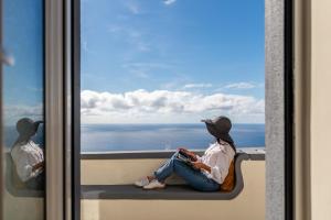 a woman sitting on a window ledge looking out at the ocean at Madeira Friendly Guest House by An Island Apart in Funchal