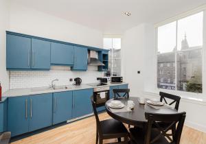 Una cocina con gabinetes azules y una mesa con sillas. en Grassmarket Apartments, en Edimburgo