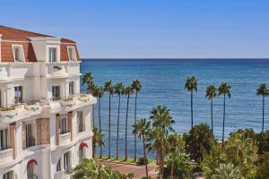 a building with palm trees and the ocean in the background at Hôtel Barrière Le Majestic Cannes in Cannes