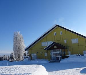 un grand bâtiment jaune avec de la neige devant lui dans l'établissement B&B Ken&Mary, à Biei
