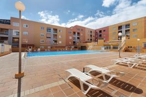a swimming pool with lounge chairs in front of a building at Apartamento Rincon Tropical in Candelaria