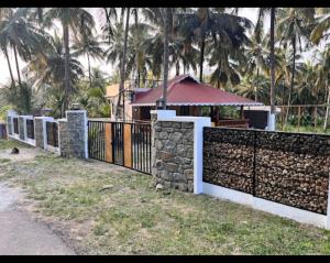 a stone fence in front of a house with palm trees at Mountain river farm resort in Agali