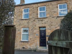 une vieille maison en pierre avec une porte noire dans l'établissement Riverside Cottage, à Warkworth