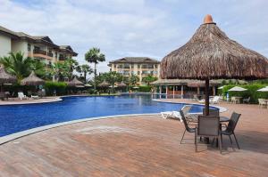a pool with chairs and a table with a straw umbrella at VG Sun Cumbuco Nascente Vista Mar 4 Pessoas in Paracumbuca