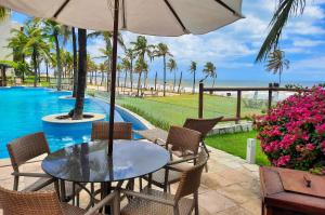 a table with chairs and an umbrella next to a pool at Wai Wai Cumbuco Vista Lateral Mar 2 Quartos in Guagiru