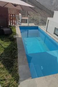 a blue swimming pool with an umbrella in a yard at Casa en cineguilla in Cieneguilla