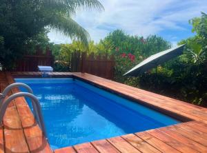 a swimming pool with a wooden deck and an umbrella at Bungalow Corossol avec piscine in Le Gosier