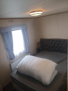 1 dormitorio con cama con almohada y ventana en Caravan on Lyons winkups holiday park, en Kinmel Bay