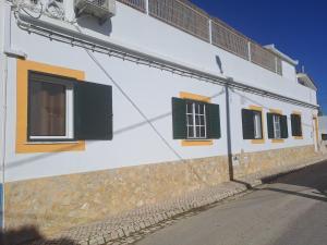 a white building with green windows on a street at Linas Guesthouse in Parchal