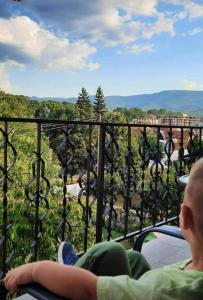 a man and a woman sitting on a balcony looking out at the mountains at Apartmani Vila Dragana Vrnjačka Banja in Vrnjci
