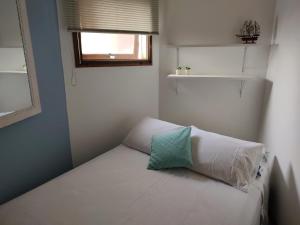 Un dormitorio pequeño con una cama blanca con una ventana. en Apto Torres com vista para o Mar, 3 suítes, sacada com churrasqueira, en Torres